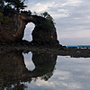 Tan Cliff Photo: A natural rock bridge is reflected in a shallow pool of seawater.